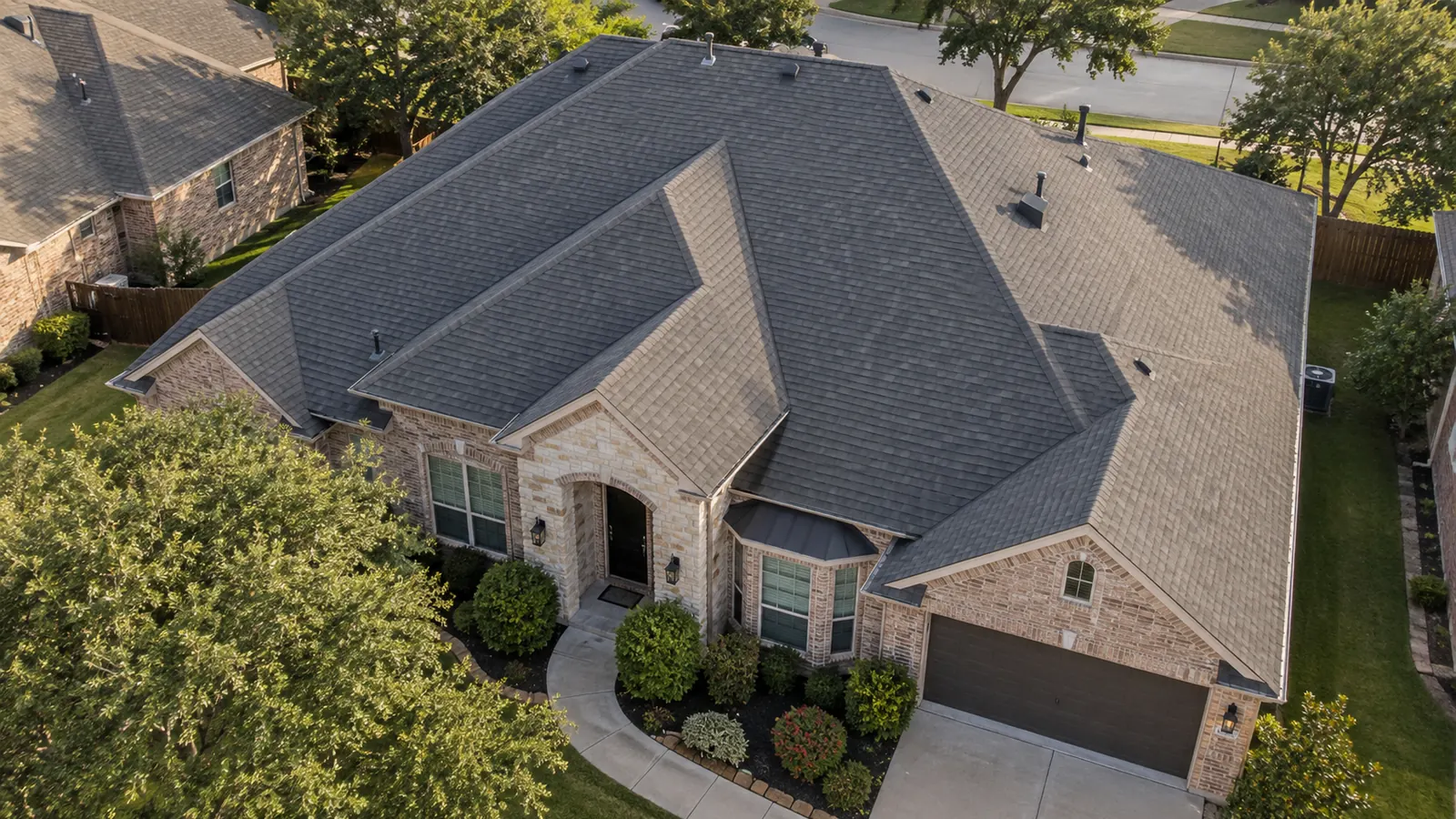 Aerial view of a home with a new dark gray architectural shingle roof, surrounded by mature trees